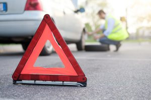 Un uomo indossa il giubbotto catarifrangente e posiziona il triangolo prima di cambiare la gomma