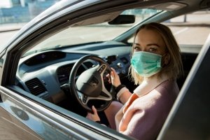 Una donna in auto con la mascherina per proteggersi dal Coronavirus
